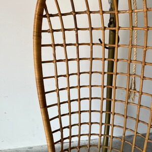 May include: A brown wicker hanging chair with a woven seat and a metal frame. The chair is suspended by a chain and rope.