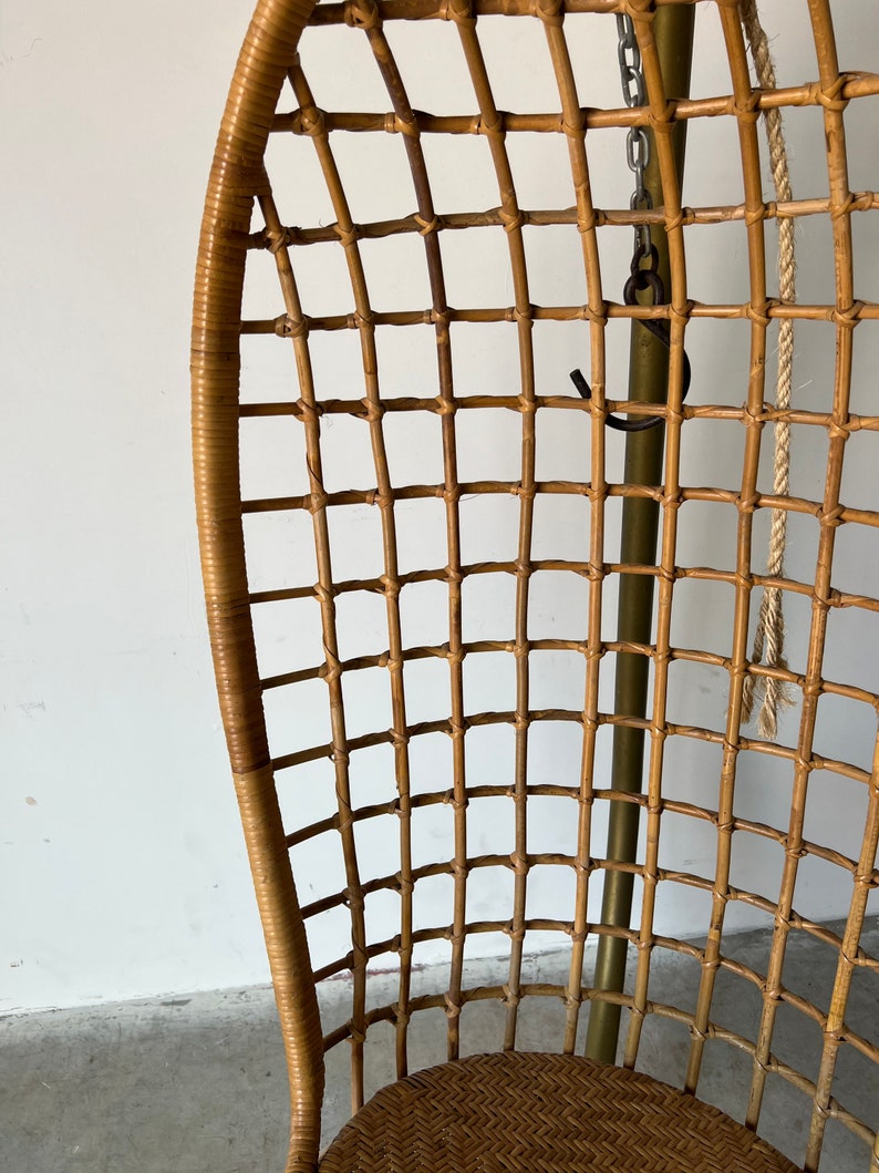 May include: A brown wicker hanging chair with a woven seat and a metal frame. The chair is suspended by a chain and rope.