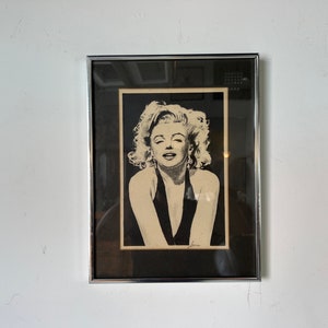May include: Black and white framed print of Marilyn Monroe in a black halter top.