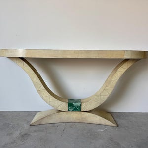 May include: A cream-colored console table with a curved base and a rectangular top. The base features a geometric pattern and a green accent. The table is approximately 60 inches long.