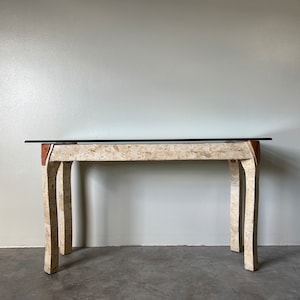 May include: A white travertine console table with a glass top. The table has four legs and a rectangular shape.