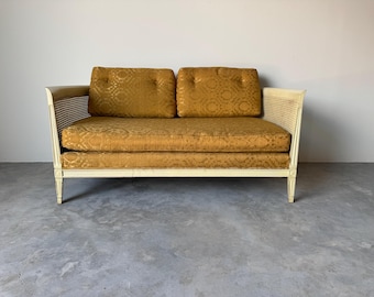 May include: A vintage loveseat with a cream-colored frame and mustard-yellow cushions. The cushions have a patterned design, and the arms feature a woven cane design. The sofa has a classic, mid-century modern style.