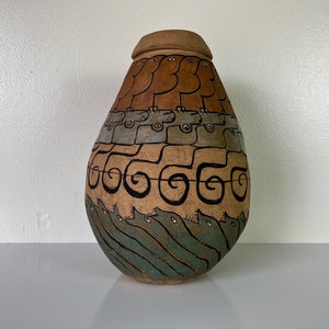 May include: A handcrafted ceramic vase with a lid, featuring a unique design. The vase is painted with brown, tan, gray, and teal colors. The design includes stylized figures, geometric shapes, and swirling patterns. The vase is a decorative item.