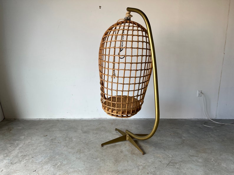 May include: A woven wicker hanging chair with a gold metal stand. The chair is suspended from the stand by a chain.