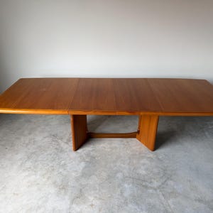 May include: A rectangular wooden dining table with a smooth, warm-toned finish. The table features a flat top with rounded edges and is supported by two wide, vertical pedestal legs connected by a horizontal base support beam.