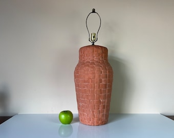 May include: A terracotta lamp with a textured, brick-like design. The lamp has a black metal shade and a gold light bulb.