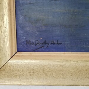 May include: A close-up of a painting's signature, "Miss Dorothy Airden", written in black ink on a blue background.