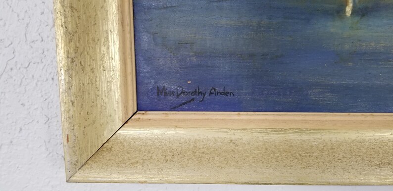 May include: A close-up of a painting's signature, "Miss Dorothy Airden", written in black ink on a blue background.