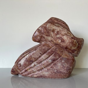 May include: Abstract sculpture carved from pink and white marble. The sculpture is abstract and has a flowing, organic shape. It is signed "J. Swan" on the side.