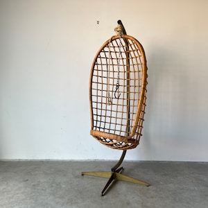 May include: A brown wicker hanging chair with a metal frame and a star-shaped base. The chair is suspended from the ceiling by a chain.