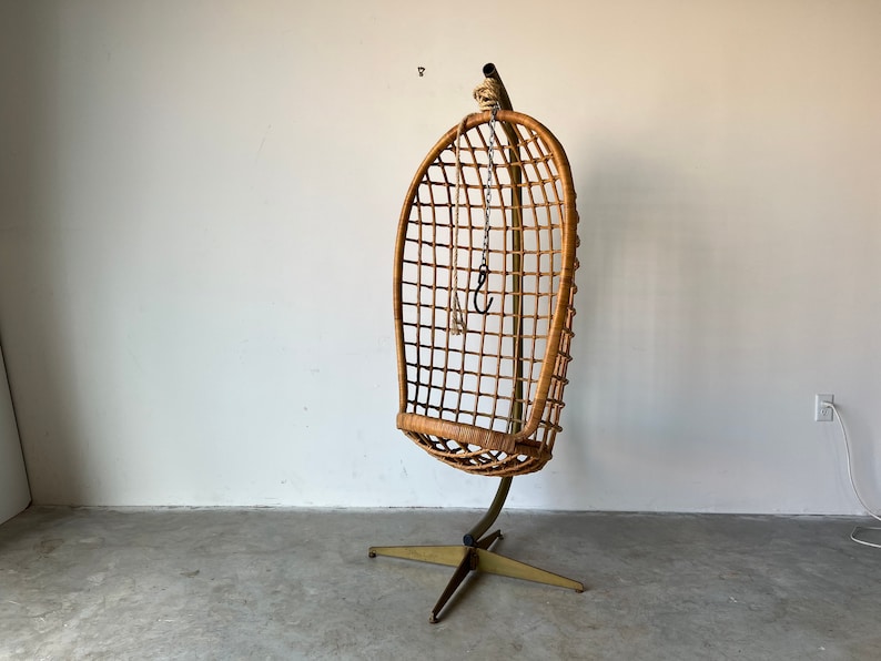 May include: A brown wicker hanging chair with a metal frame and a star-shaped base. The chair is suspended from the ceiling by a chain.