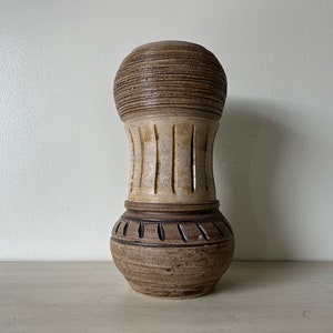 May include: A brown and white ceramic vase with a textured surface and a unique design. The vase has a wide mouth and a narrow base.