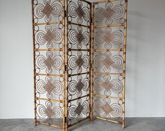 May include: A three-panel room divider made of woven bamboo. The divider has a natural brown color with decorative geometric patterns. The panels are connected by hinges, allowing for flexible positioning. The divider stands upright on a concrete floor.