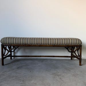 May include: A rectangular bench featuring a dark brown bamboo frame with intricate branch-like supports. The seat is upholstered in a fabric with a vertical striped pattern in shades of tan, brown, grey, and cream, providing a firm, flat surface.