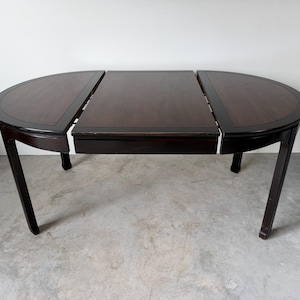 May include: A dark brown wooden dining table with a smooth, polished surface and a rectangular center leaf section flanked by two semi-circular ends. The table features four sturdy legs and a clean, structured design with visible seams between the sections.
