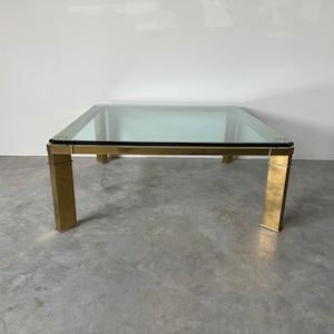 May include: A square glass top coffee table with a gold metal frame. The table has a simple, modern design.