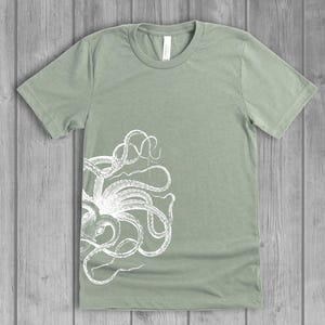 A dusty light sage green women's short-sleeve t-shirt with a white side octopus with tentacles print on the front.