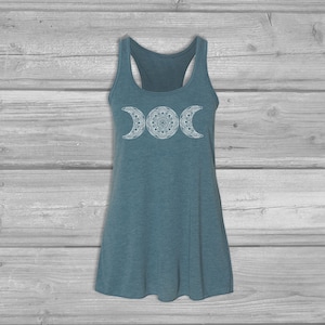 May include: A teal blue tank top with a white triple moon mandala design. The tank top has a racerback style.