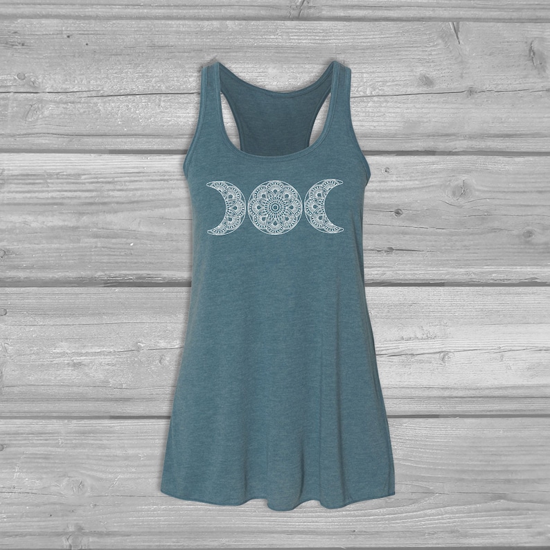 May include: A teal blue tank top with a white triple moon mandala design. The tank top has a racerback style.