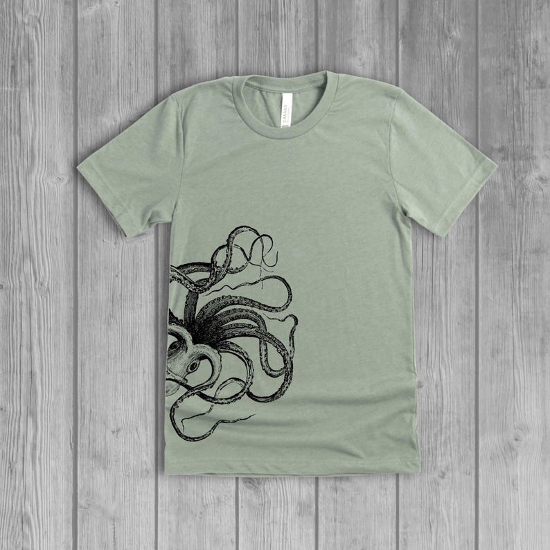 A dusty light sage green women's short-sleeve t-shirt with a black side octopus with tentacles print on the front.