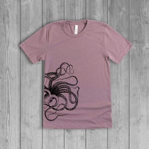A dusty light mauve pink women's short-sleeve t-shirt with a black side octopus with tentacles print on the front.