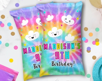 May include: Two party favor bags with a tie-dye design in shades of purple, yellow, and green. The bags feature cartoon clouds and the text "Maddi Maddison's 9th Birthday!" in bright colors. Confetti and party supplies surround the bags.