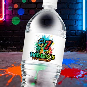 Pode incluir: Uma garrafa de água de plástico transparente com um rótulo branco com o texto "67 Maddox's 5th Birthday" em um estilo de grafite colorido. O fundo inclui uma parede de tijolos e respingos de tinta.