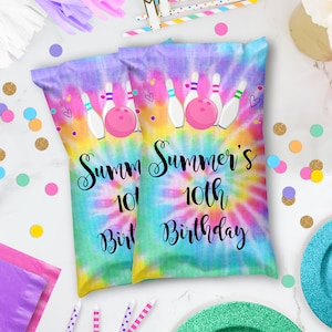 May include: Two tie-dye party favor bags with bowling pins and a bowling ball. The bags are decorated with hearts and confetti. The text on the bags reads "Summer's 10th Birthday".