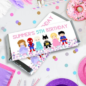 以下が含まれることがあります： 「SUMMER'S 5TH BIRTHDAY」の文字と漫画のキャラクターが描かれたチョコレートバーの包装紙。キャラクターには、プリンセス、スパイダーマン、エルサ、バットマン、別のプリンセス、スーパーマンが含まれます。包装紙は紙吹雪で飾られています。