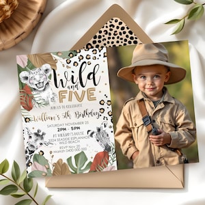 Puede incluir: Una invitación de cumpleaños con temática de selva con una foto de un niño pequeño con un sombrero de safari y sosteniendo una cámara. La invitación presenta un león, una cebra, una jirafa y plantas verdes frondosas. El texto de la invitación dice "Wild and Five" e incluye detalles sobre la fiesta de cumpleaños, incluida la fecha, la hora y la ubicación.