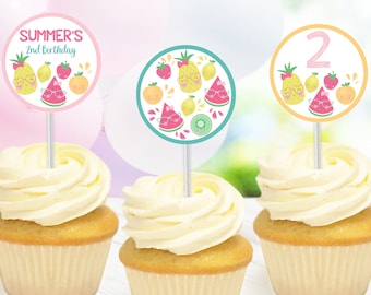 May include: Three cupcakes with white frosting topped with round fruit-themed cupcake toppers. The toppers feature a pineapple, watermelon, lemon, and strawberry with sunglasses. One topper says "SUMMER'S 2nd Birthday" and another says "2".