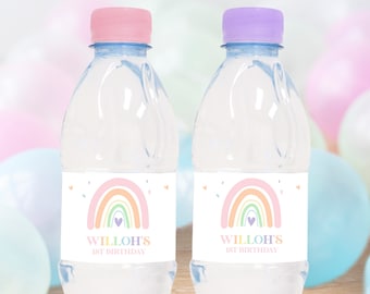 May include: Two clear plastic water bottles with rainbow labels. The labels feature a pastel rainbow with a heart in the center and the text "WILLOH'S 1ST BIRTHDAY". The bottles have pink and purple lids.