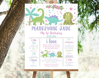 May include: A colorful dinosaur-themed first birthday sign with the name Madelynne Jade and the date 09.08.20XX. The sign lists the child's age, height, weight, number of teeth, favorite foods, favorite book, nickname, first word, and abilities.