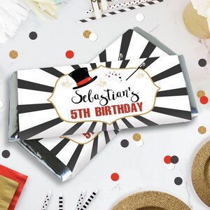 May include: A chocolate bar wrapper with a black and white striped design. The label features a top hat, playing cards, and a magic wand. Text reads "Sebastian's 5th Birthday" in a decorative font.