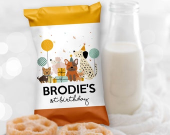May include: A yellow and orange party favor bag with a white background. The bag features a cartoon illustration of dogs wearing party hats and holding presents. The text "BRODIE'S 1st birthday" is printed on the bag.