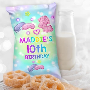 May include: A colorful party favor bag with the text "MADDIE'S 10th BIRTHDAY" in bright colors. The bag features illustrations of pajamas, a sleep mask, and stars. A glass bottle of milk and fried pastries are in the background.