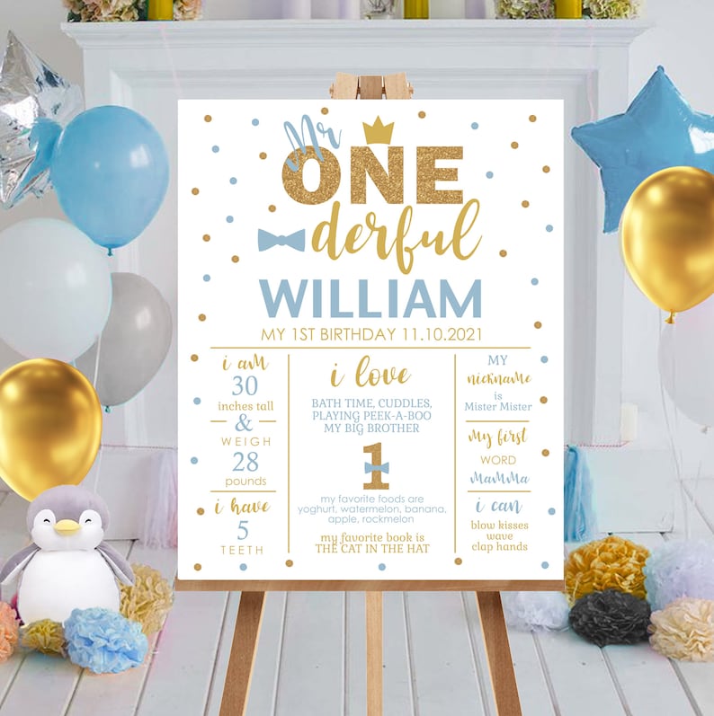 May include: A white and gold birthday sign for a one-year-old boy named William. The sign features a gold crown, a bow tie, and the words "Mr. One-derful". The sign also includes details about the child's age, height, weight, favorite foods, and favorite book.