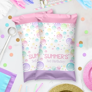 May include: Two pink and purple favor bags with a white background and a colorful bubble pattern. The bags have a purple border and the text "SUMMER'S 3rd Birthday!" printed on them.