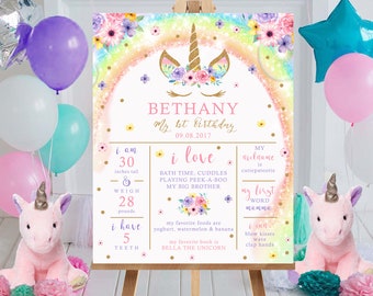 May include: A pink and white unicorn birthday sign with a rainbow background. The sign says "Bethany My 1st Birthday 09.08.2017". It also lists Bethany's age, height, weight, favorite foods, first word, and other milestones.
