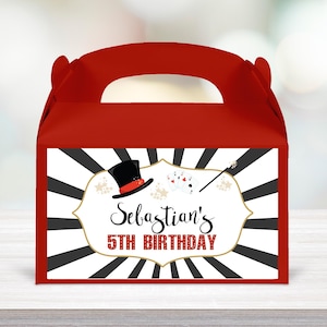 May include: Red party favor box with a handle. The front features a white label with a black and gold design, a top hat, playing cards, and a magic wand. The text reads "Sebastian's 5th Birthday."
