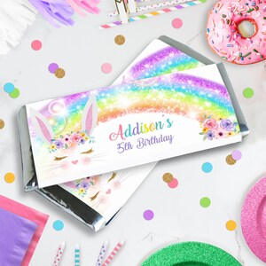 May include: A white chocolate bar wrapper with a rainbow, glitter, and a cute bunny with flowers. The text on the wrapper says "Addison's 5th Birthday".