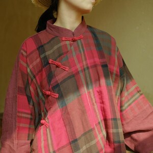 May include: A red, brown, and blue plaid shirt with a mandarin collar and decorative knotted closures. The long-sleeved shirt has a relaxed fit and is made of a soft, woven fabric. The shirt is a unique, vintage-inspired garment.