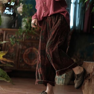 May include: Wide-leg corduroy trousers in a dark burgundy and green floral pattern, paired with a long-sleeved button-down shirt in a solid muted red. The trousers feature a relaxed fit with cuffed hems and a textured, ribbed fabric surface.