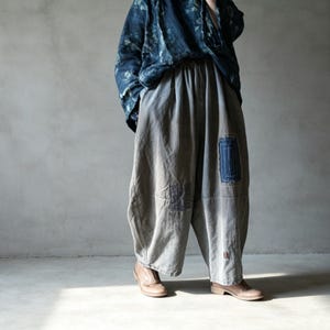 Peut inclure: Pantalon gris ample doté d'une taille élastique et de patchs rectangulaires bleus visibles avec des détails de surpiqûres blanches. Le pantalon présente une coupe large et est associé à une chemise à manches longues bleu foncé à motifs.