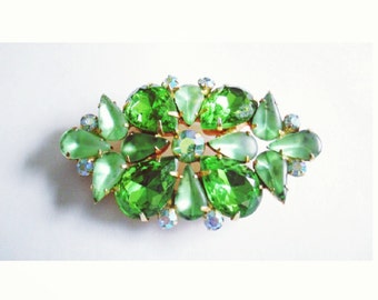 Pode incluir: Um broche de strass verde e transparente com um design floral.