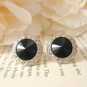 May include: A pair of silver earrings with black gemstone accents. The earrings are round and have a decorative border.
