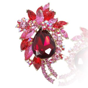 Peut inclure: Une broche en forme de larme rouge avec de plus petits strass roses et rouges disposés en forme de fleur.
