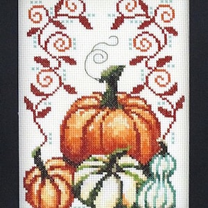Könnte beinhalten: Kreuzstich-Stickerei mit einer Herbst-Ernte-Szene mit drei Kürbissen. Die Kürbisse sind orange, grün und weiß mit einem braunen Stiel. Der Hintergrund ist weiß mit einem roten und orangefarbenen Blumendesign.