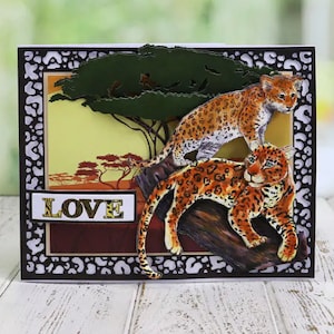 Könnte beinhalten: Eine Grußkarte mit schwarzem Rand und Leopardenmuster. Die Karte zeigt eine Dschungelszene mit zwei Leoparden und einem Baum. Das Wort "LOVE" ist in goldenen Buchstaben auf der Karte geschrieben.