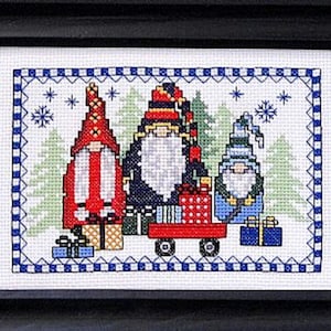 Könnte beinhalten: Drei Gnome mit roten, blauen und schwarzen Mützen ziehen einen roten Wagen voller Geschenke. Die Gnome stehen vor einer verschneiten Waldlandschaft mit Schneeflocken.